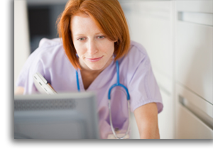 A nurse beding over a computer for patient information.